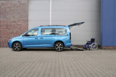 Blauer VW Caddy von der Seite mit geöffneter Heckklappe und Rollstuhl