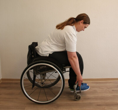 Rollstuhlfahrerin bei einer Fitnessübung nach vorne gebeugt