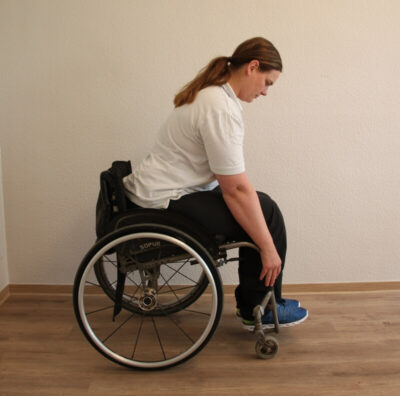 Rollstuhlfahrerin bei einer Fitnessübung nach vorne gebeugt