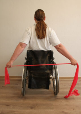 Rollstuhlfahrerin mit Fitnessband bei einer Übung