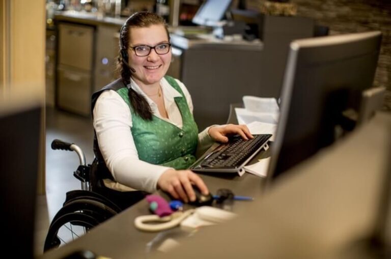 Frau im Rollstuhl an der Rezeption eines Hotels arbeitet am Computer