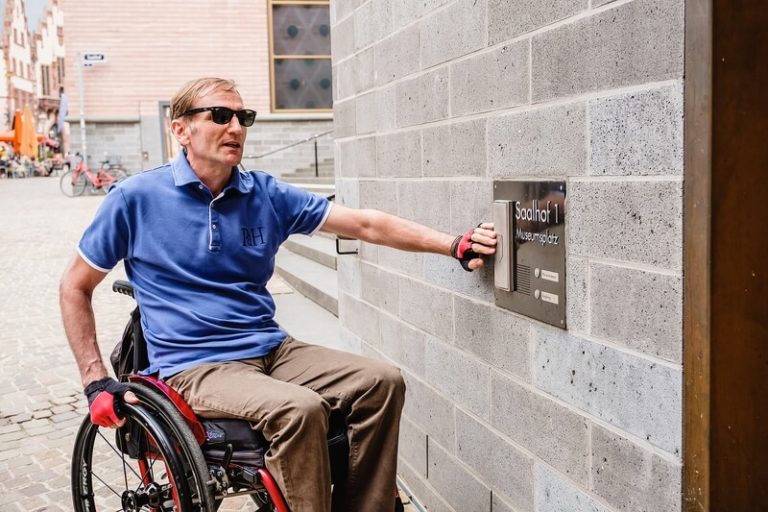 Blinder Rollstuhlfahrer an einem Klingelschild