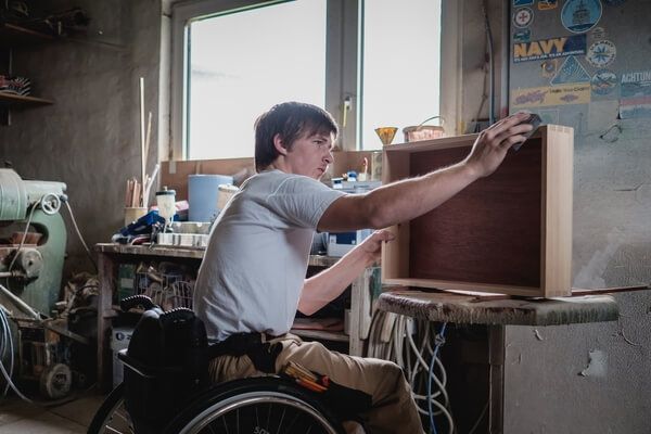 Junger Mann im Rollstuhl arbeitet in einer Schreinerei