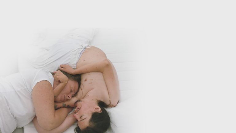Zwei liegende Menschen mit naktem Oberkörper umarmen sich