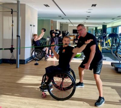 Mann im Rollstuhl macht Sport mit Unterstützung eines Physiotherapeuten