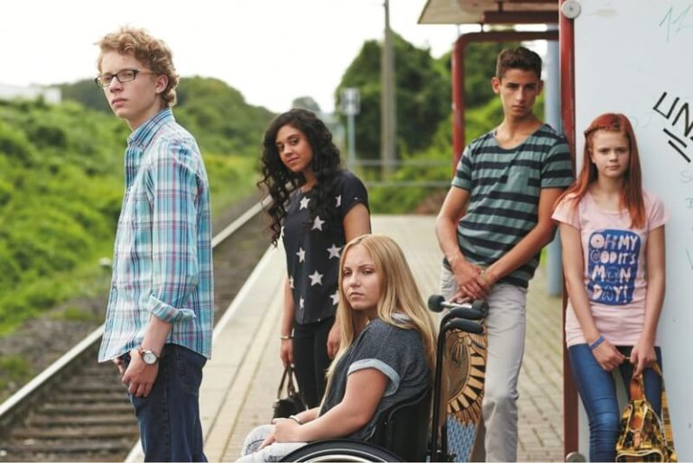 Junge Menschen, darunter eine Rollstuhlfahrerin, stehen am Bahnhof