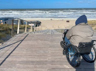 Rollstuhlfahrer von hinten an einer steilen Rampe, die zum Strand führt