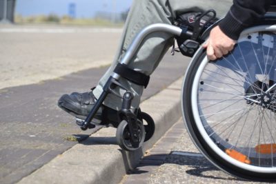 Man sieht die Vorderräder eines manuellen Rollstuhls, die etwas angehoben sind, damit der Nutzer eine flache Kante hinauffahren kann.