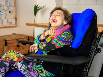 Man sieht ein lachendes Mädchen mit Behinderung in einem Rollstuhl