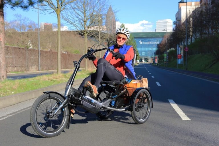 Eine Frau mit Helm sitzt auf einem Dreirad und lächelt in die Kamera