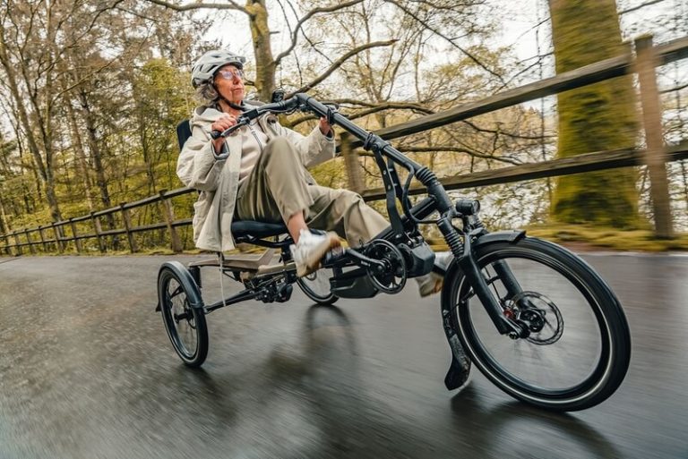 Ältere Frau mit Helm fährt auf einem dreirädrigen Fahrrad