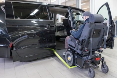 Man sieht einen Van von der Seite mit einer Unterflurrampe, über die ein Rollstuhlfahrer ins Fahrzeug gelangt.